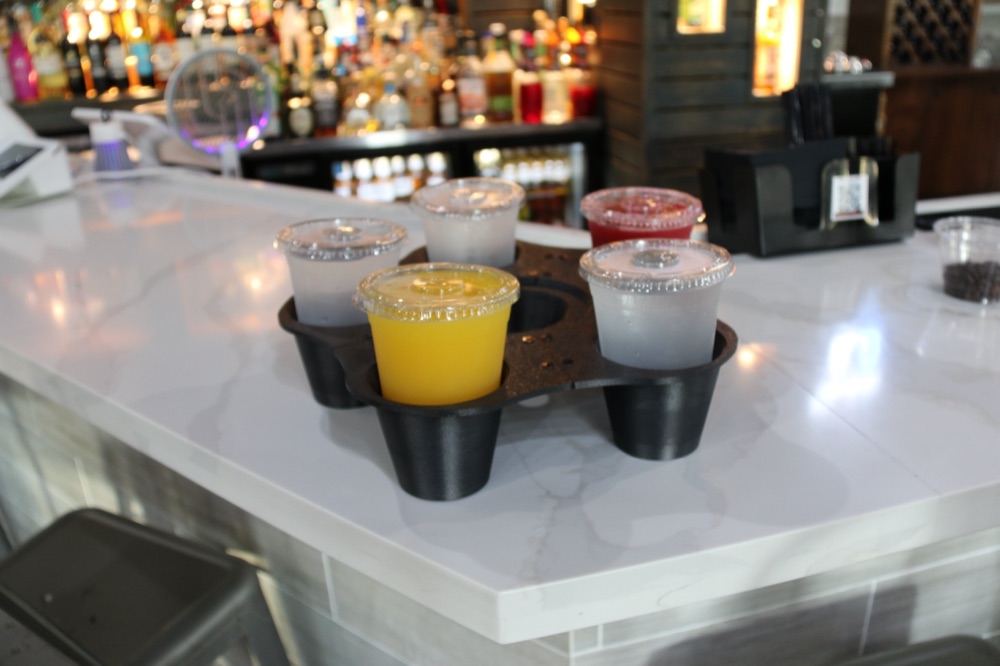 GrippyTray resting on a bar rail mid-service, in front of a lit spirits shelf