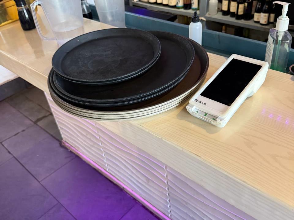 A stack of worn flat serving trays piled on a bar counter